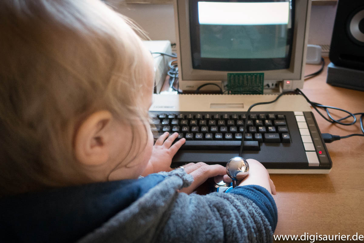 Kleinkind sitzt an einem alten 8-Bit-Computer und drückt einen Joystick-Knopf